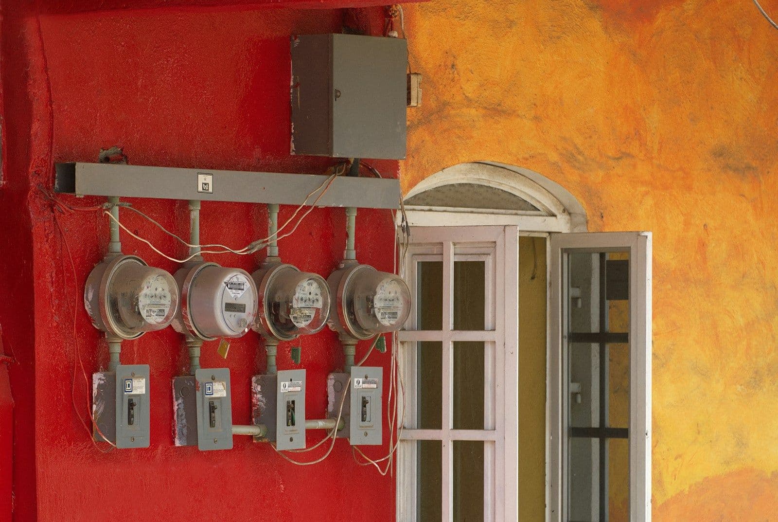 Four electric meters mounted on a red wall, representing choosing between electricity providers