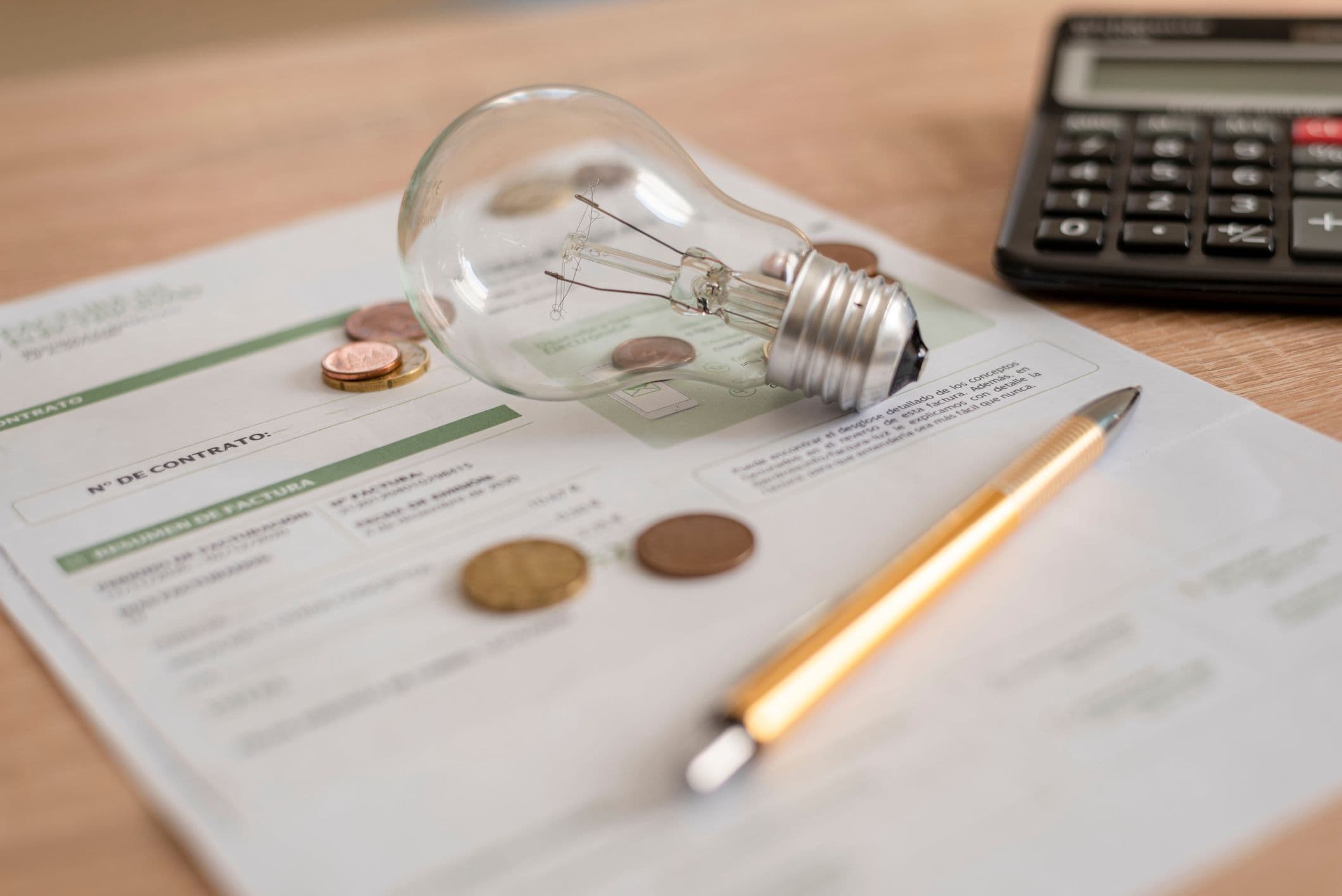 Light bulb and coins resting on an electricity bill with a calculator and pen, representing the gap between advertised and actual electricity costs